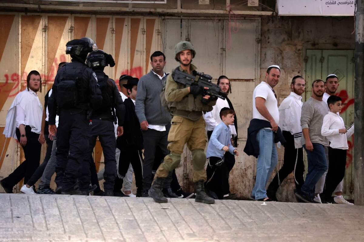 Israeli security forces stand guard as Jewish settlers look toward Palestinian residents, on their way to visit the tomb of Othniel ben Kenaz in the area H1 (controlled by Palestinian authorities), in the occupied West Bank city of Hebron, on November 19, 2022 (Photo by HAZEM BADER / AFP)