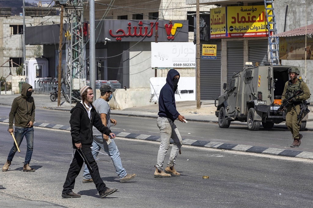 Israeli settlers walk with batons as they cross a street during clashes in which Israeli settlers attacked Palestinian residents and shops in the town of Huwara in the occupied West Bank on October 13, 2022. (Photo by Oren ZIV / AFP)