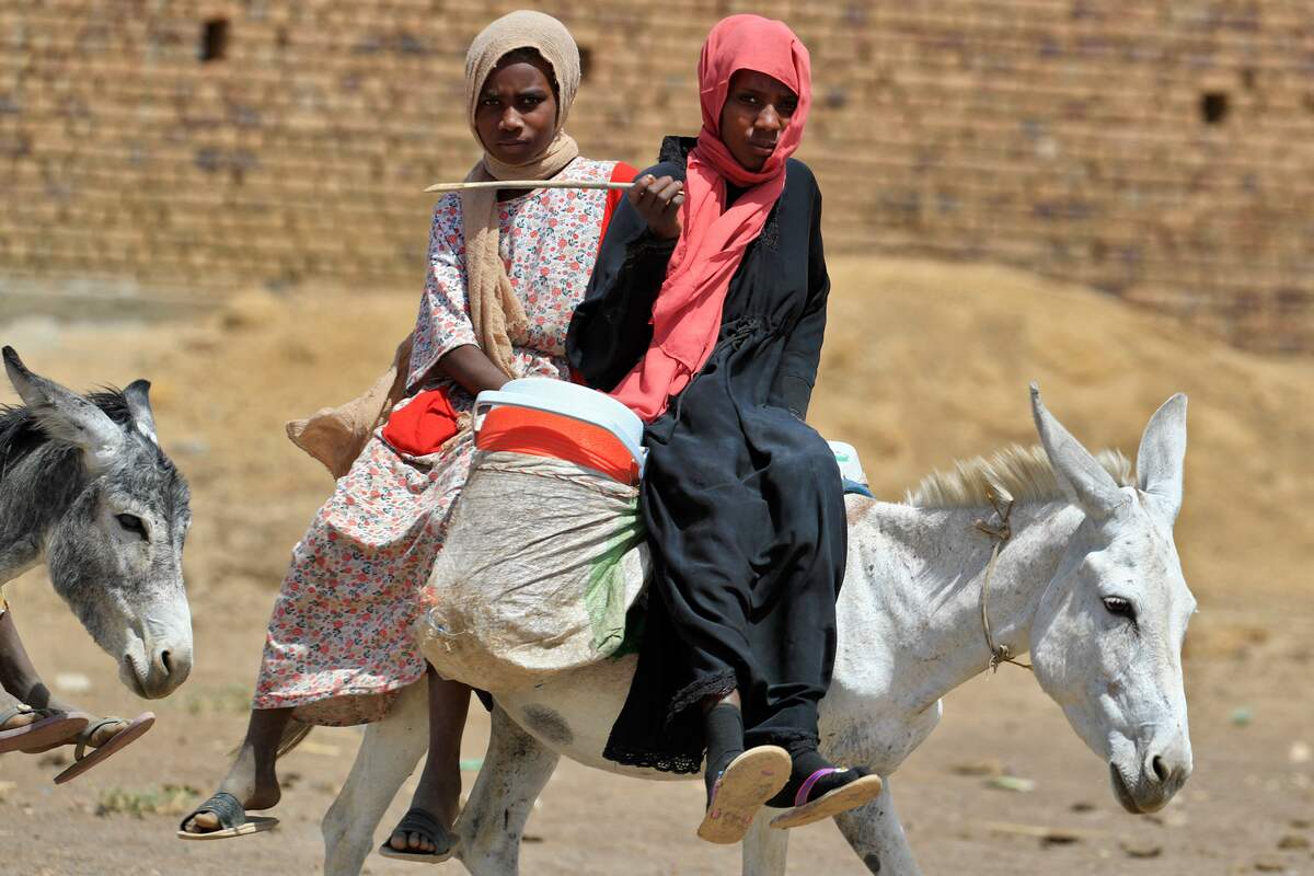 Sudanese women ride their donkeys in the village of al-Laota, about 70 kilometres southwest of Sudan's capital Khartoum on May 28, 2022. Impoverished Sudan has for years been grappling with a grinding economic crisis, which deepened after last year's military coup prompted Western governments to cut crucial aid. The October coup derailed a fragile transition put in place following the 2019 ouster of president Omar al-Bashir. (Photo by ASHRAF SHAZLY / AFP)