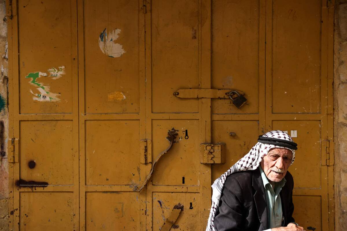 A man sits in front of a closed shop in a market area in the occupied West Bank city of Hebron on February 23, 2023, during a general strike called to protest against the Israeli raid of Nablus. Eleven Palestinians were killed and more than 80 wounded by gunfire on February 22 when Israeli troops raided the flashpoint West Bank city of Nablus, drawing international appeals for calm. (Photo by HAZEM BADER / AFP)