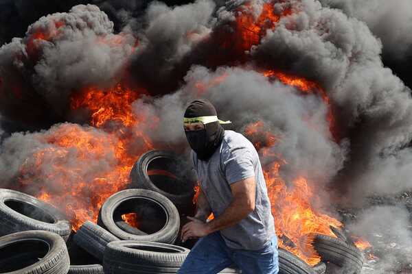 TOPSHOT - A protester runs near burning tyres during clashes with Israeli forces following a demonstration against the expropriation of Palestinian land by Israel in the village of Kfar Qaddum, in the occupied West Bank on September 29, 2023. (Photo by Jaafar ASHTIYEH / AFP)