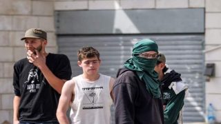 Israeli settlers look on as they stand along a street in the town of Huwara near Nablus in the occupied West Bank on February 27, 2023. Two Israelis living in the Har Bracha settlement near Nablus were killed on February 26 in a Palestinian attack, officials said, sparking violence in which a Palestinian man was killed, while settlers torched homes and vehicles in revenge. (Photo by RONALDO SCHEMIDT / AFP)